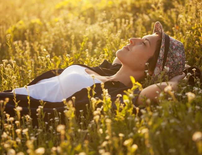The girl in a hat dremet among wildflowers at sunset